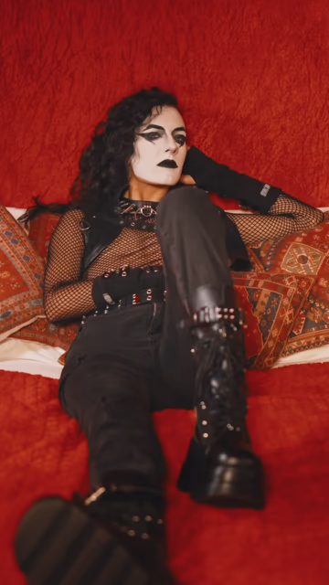 Shonalika dressed in industrial gear and whiteface beckons from a bed. the footage cuts to a separate scene with the band dressed more casually and performing in a sort of grungey looking space. the video cuts back to the first scene where Shonalika is now doing their makeup in a mirror and looking very self-satisfied